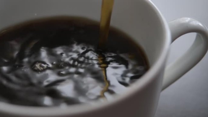 新鲜的早晨倒在红茶上特写。选择性聚焦。从咖啡机特写镜头中倒入杯中的咖啡的慢动作俯视图。慢动作将黑咖啡
