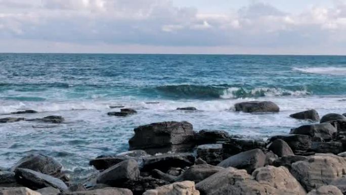 海浪溅落在蓝色海洋背景的岩石海岸上。波涛汹涌的岩石海岸线在暴风雨中席卷而来。海浪用泡沫在石头上破裂。