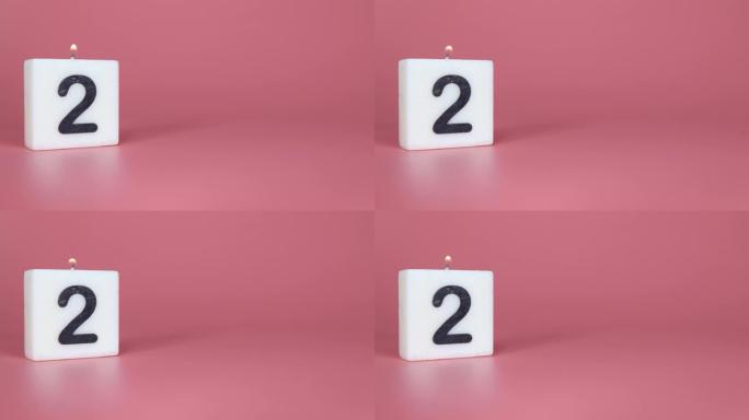 一根方形蜡烛，上面写着数字2在庆祝生日或周年纪念日的粉红色背景上被点燃和吹灭