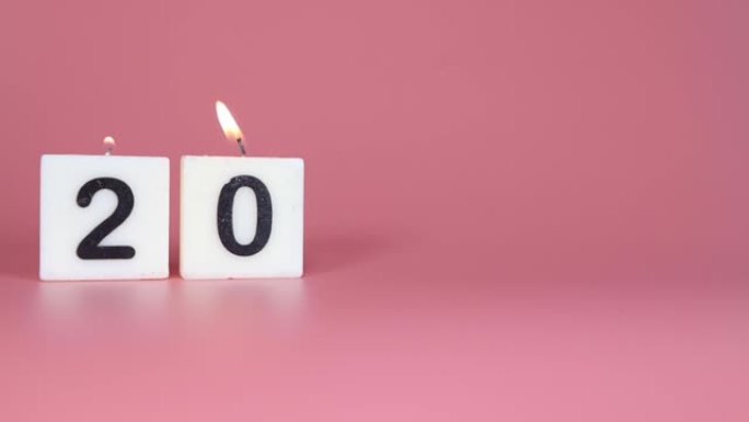 一根方形蜡烛，上面写着数字20被点燃并在庆祝生日或周年纪念日的粉红色背景上吹灭
