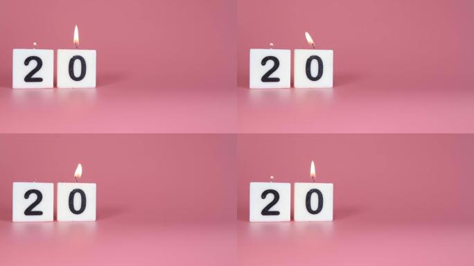 一根方形蜡烛，上面写着数字20被点燃并在庆祝生日或周年纪念日的粉红色背景上吹灭