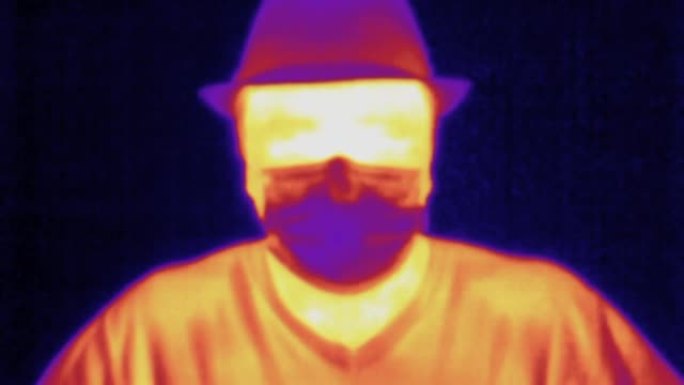 紫外光谱热成像相机。戴帽子的男人，戴上防护医用口罩，看热像仪和手势你好。检测体温升高的Covid大流