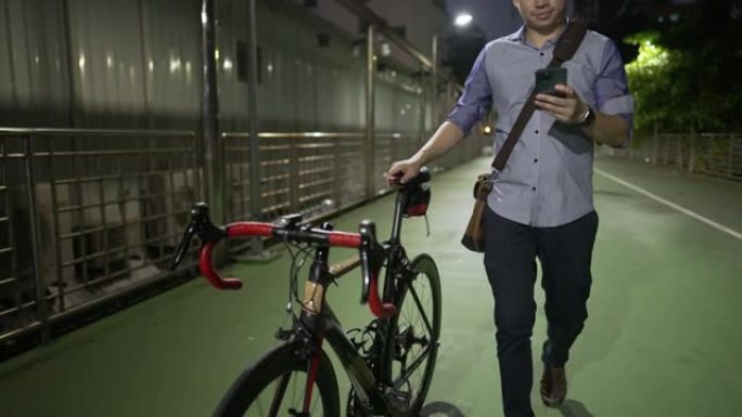 亚洲年轻成年男性在深夜公司加班后骑自行车回家时使用手机，自由职业者在空荡荡的步行街上独自一人回家，找