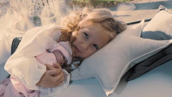 孩子在睡觉。可爱的小女孩。美丽的小公主抱着洋娃娃，躺在窗户附近的枕头上。晴天