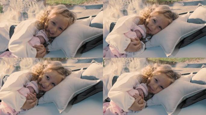 孩子在睡觉。可爱的小女孩。美丽的小公主抱着洋娃娃，躺在窗户附近的枕头上。晴天