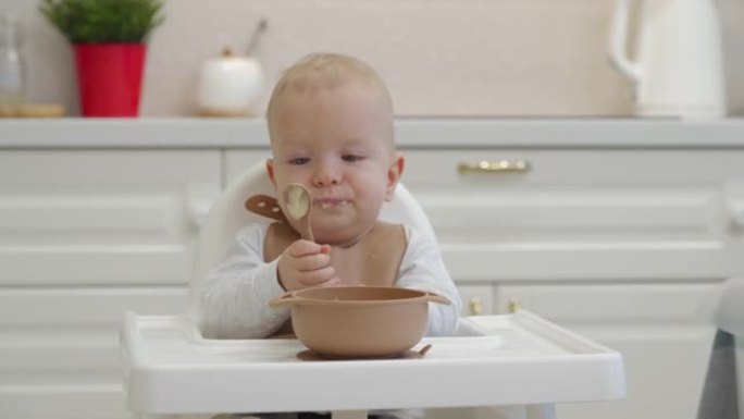 孩子吃粥，蹒跚学步的孩子用勺子学习吃饭，微笑的孩子用食物弄脏了脸。