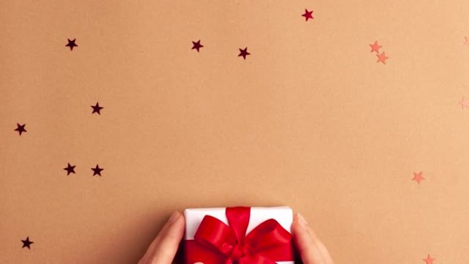 带有红色袖子的人的手拿走了一张白纸礼物，上面有一个红色缎带蝴蝶结，棕色背景上有红色星星。定格动画圣诞