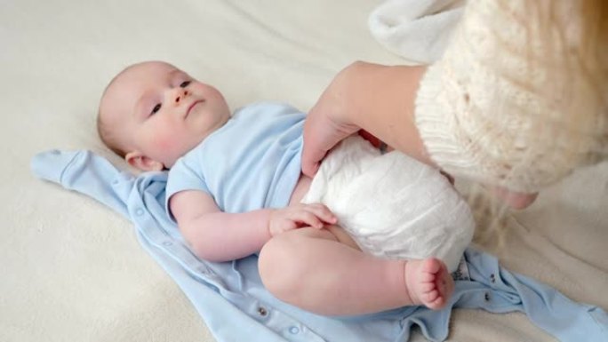 年轻的母亲给躺在床上的小儿子穿上新的干净尿布。父母、婴儿卫生和儿童发展的概念