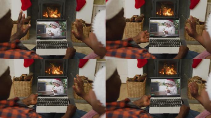 非洲裔美国夫妇戴着圣诞老人的帽子，使用笔记本电脑与屏幕上的男孩进行圣诞节视频通话