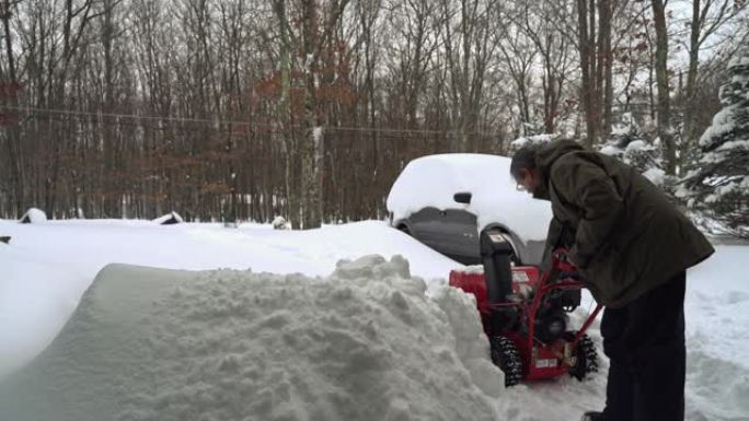 一名男子在冬季暴风雪后清理了被雪覆盖的汽车周围的车道，启动了现在的吹瓶机