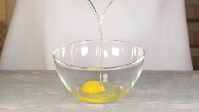 特写镜头: 黑手套的手将鸡蛋打碎成透明的杯子，在家里的木桌上准备食物，全高清。蛋黄正在掉进玻璃弓里。