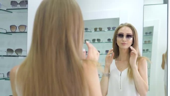 一家光学商店里的一个年轻漂亮的女孩拿起透明眼镜看视觉。女人手中的薄框时尚眼镜。女孩戴上眼镜。医疗保健