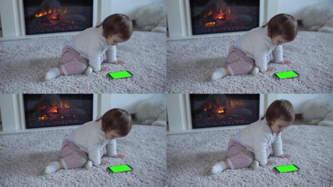 可爱开朗的幸运聪明的学步宝宝女孩在蓬松的地毯上使用智能手机绿屏手机Hromakey看视频卡通放松在家