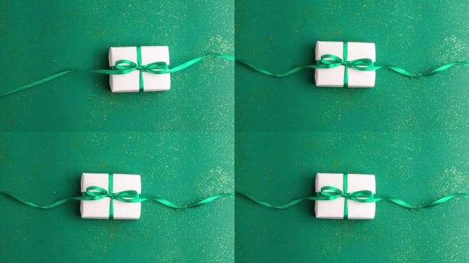 白色礼品盒，绿色背景上有翠绿色缎带蝴蝶结，金色闪光。定格动画圣诞假期和呈现概念平铺与复制空间