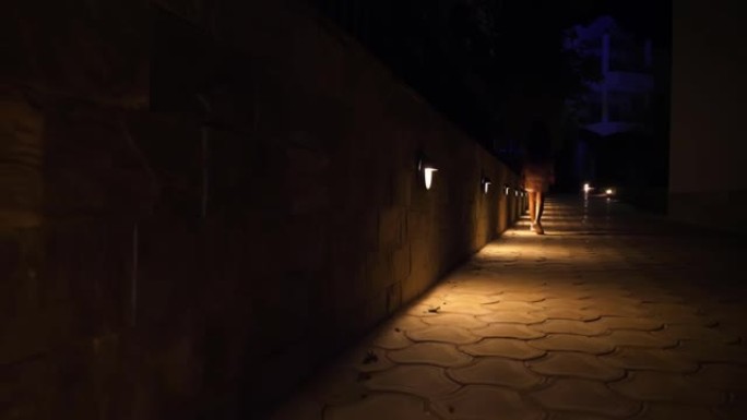 晚上散步。晚上有灯的小路。特写。穿着运动鞋的女性腿沿着小路行走。花园灯笼，灯光位于小径上