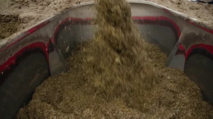饲料喂养动物的准备，挖掘机铲斗将复合饲料倒入大型搅拌机中，农场过程的特写