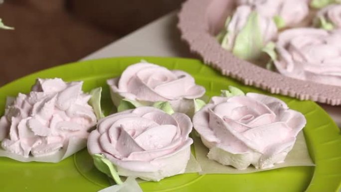 一个女人用糕点袋在棉花糖玫瑰上做花瓣。托盘上摆放着不同形状的棉花糖。特写镜头