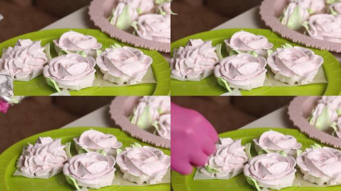 一个女人用糕点袋在棉花糖玫瑰上做花瓣。托盘上摆放着不同形状的棉花糖。特写镜头
