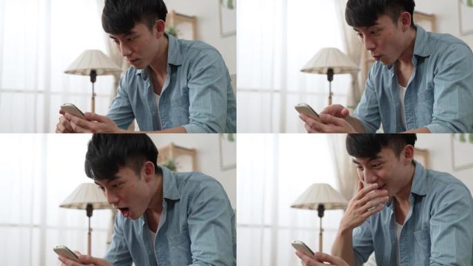 特写一位震惊的台湾男性在手机屏幕上张开嘴向下滚动，同时在家里的手机上阅读令人惊讶的在线新闻。