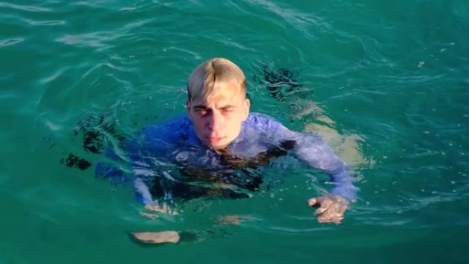 一个穿着衬衫和领带的有趣男人在阳光明媚的日子在海里游泳。慢动作，4k