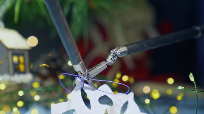 机械臂的微小爪子将线绑在纸雪花上。设备的精确运动。背景下的圣诞装饰品。