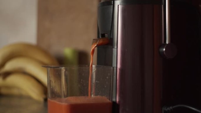4k离心榨汁机压榨自制胡萝卜汁。用果汁填充塑料杯。制作鲜榨果蔬汁，特写。厨房电器。健康饮料，香蕉，早