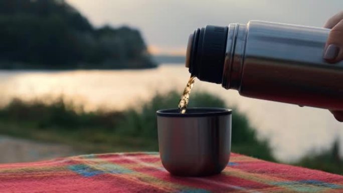秋季公园室外热杯倒入热茶。红领巾秋季野餐保温瓶
