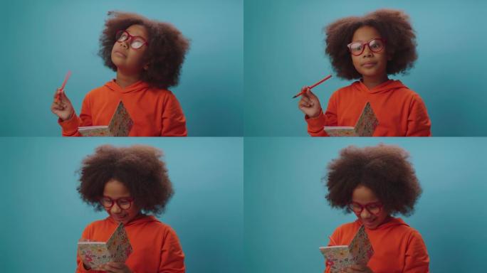 戴眼镜的漂亮非洲裔美国女孩有一个主意，并在笔记本上写下。聪明的孩子手里拿着笔记本和铅笔。