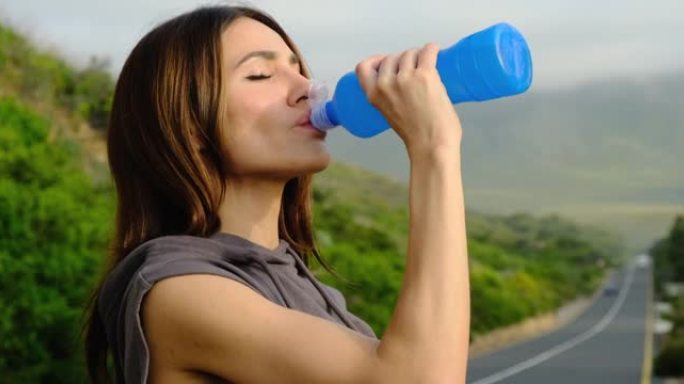 健身女子站在路上锻炼后从瓶子里喝水