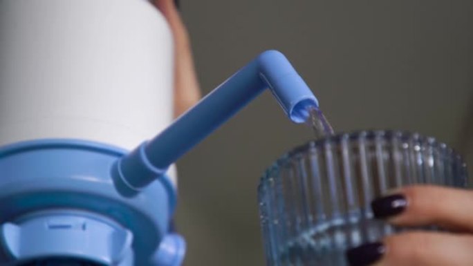 女人在家里的厨房里按压力将水从一个大瓶子里泵入蓝色玻璃杯中