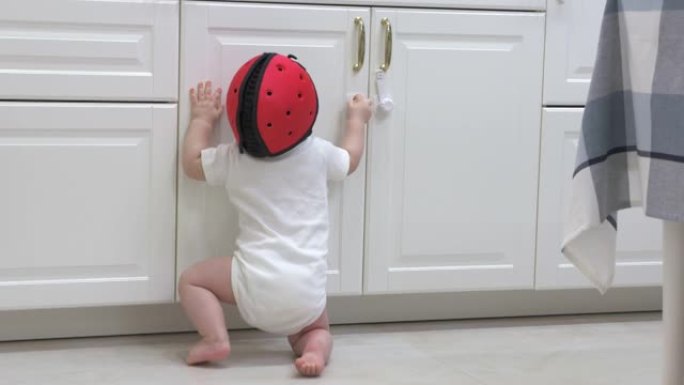 好奇的小孩戴着安全帽探索厨房橱柜，孩子试图用婴儿安全锁打开厨房橱柜门。
