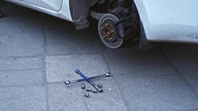 汽车轮毂，在车库车间轮胎更换过程中暴露出制动盘和制动片，凸耳螺母和扳手铺设在地面上