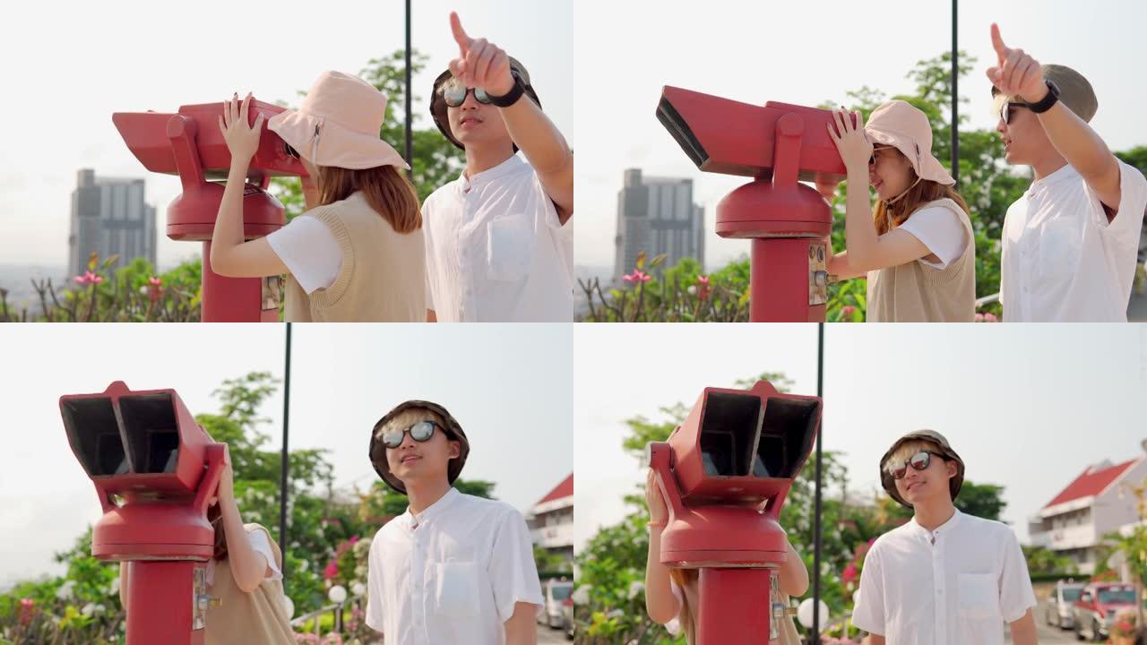 欢快的亚洲年轻夫妇游客在观看点使用投币式双筒望远镜观看城市背景