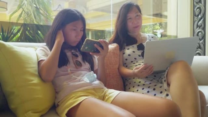 亚洲母亲在酒店大堂使用笔记本电脑与女儿一起度假，在任何生活方式概念的地方工作。