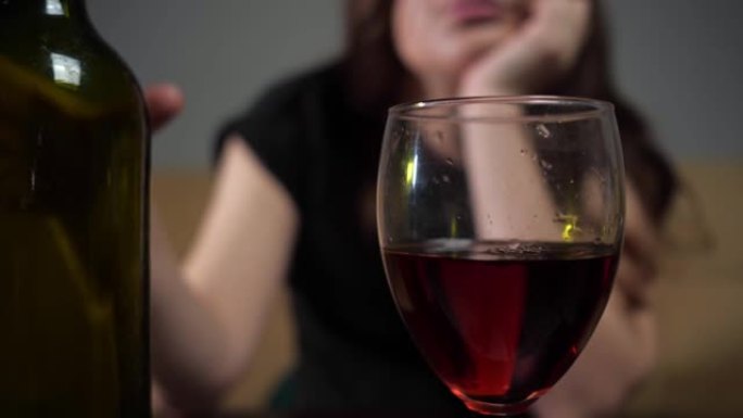 醉醺醺的女人带着悲伤的脸将葡萄酒倒入酒杯中