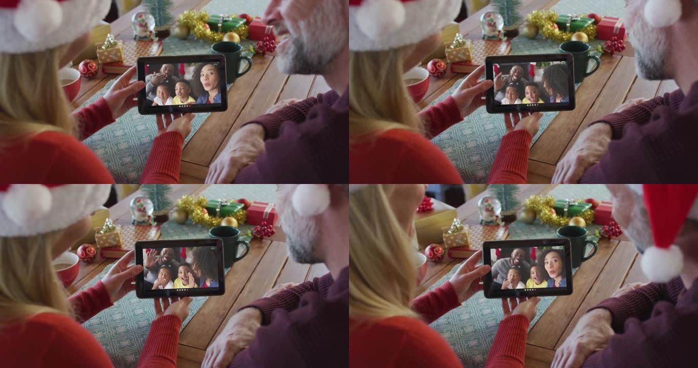 微笑的高加索夫妇戴着圣诞老人帽子，使用平板电脑与家人在屏幕上进行圣诞节视频通话