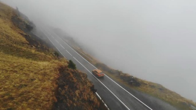 橙色汽车在秋天穿越雾山公路。秋季乡村路线自动驾驶的航拍。SUV通过风景优美的方式行驶。旅程的概念。顶