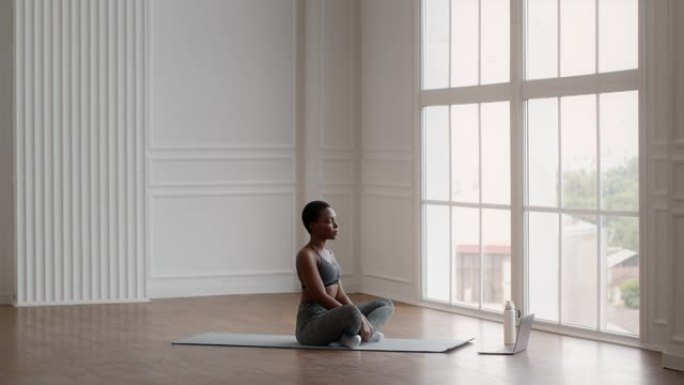 在线瑜伽。运动型黑人女性在笔记本电脑上打开视频课，开始冥想练习