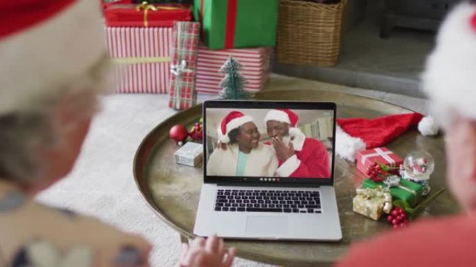 戴着圣诞老人帽子的高级高加索夫妇使用笔记本电脑进行圣诞视频通话，屏幕上有夫妇