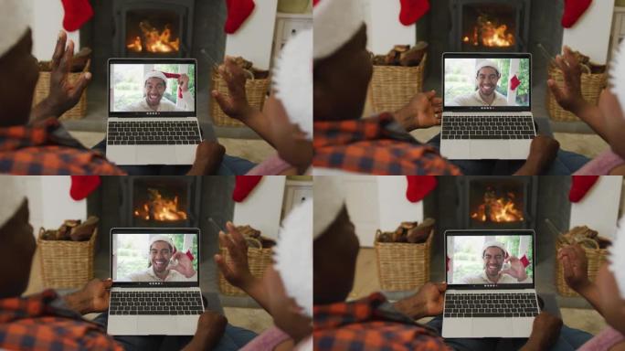非裔美国人夫妇戴着圣诞老人的帽子，使用笔记本电脑与屏幕上的男人进行圣诞节视频通话