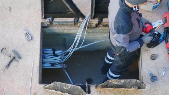 工人用电动拆除锤在光缆线路的钢筋混凝土竖井中闯入。开放式三角形铸铁井盖