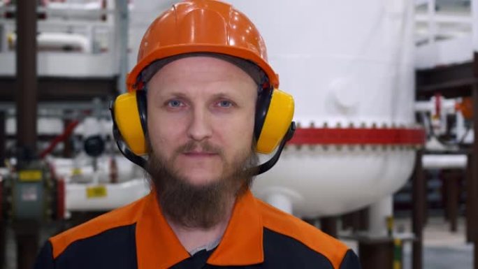 在燃料气制备单元的工作场所，一个戴着工作头盔和防护耳机的男人的特写镜头。工业生产中的工作