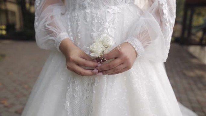 身着白色婚纱的新娘手持婚礼花束在户外，等待着她心爱的新郎