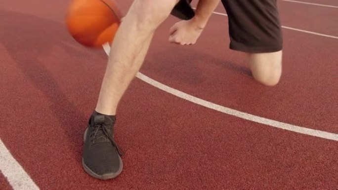 腿部男子通过在室外球场上两腿之间滚动篮球来练习球技，摄像机跟踪