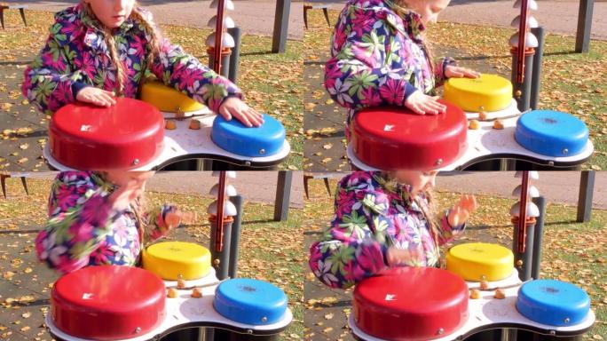 一个小女孩在秋天城市公园的操场上用手敲着邦戈鼓。孩子玩音乐与彩色彩虹儿童鼓设置在秋天的街道。可爱快乐