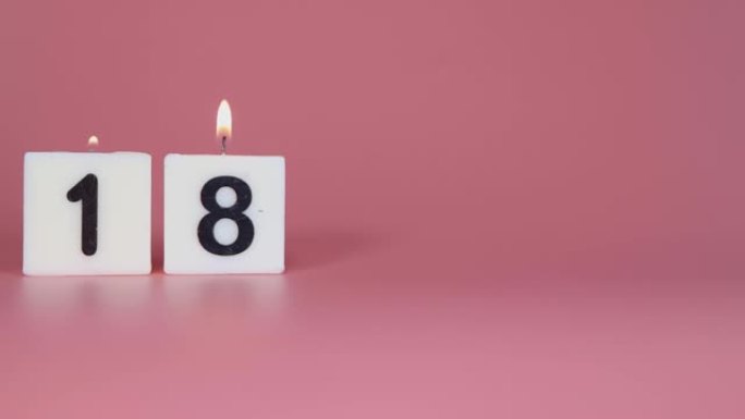 一根方形蜡烛，上面写着数字18在庆祝生日或周年纪念日的粉红色背景上被点燃和吹灭
