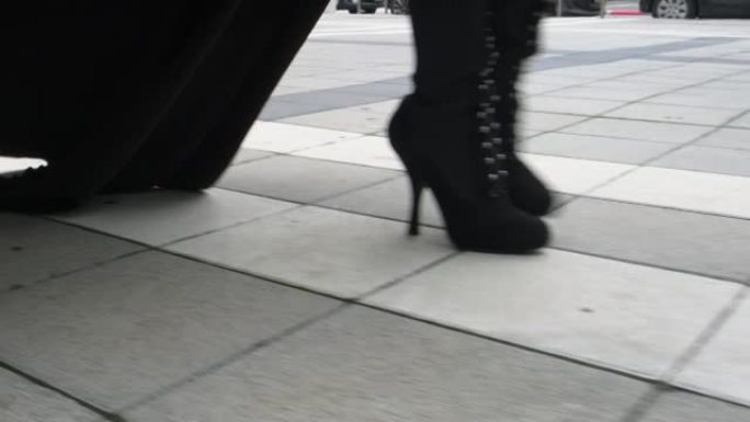 穿着黑白鞋子的模特的女性腿沿着瓷砖城市道路在城市中行走。