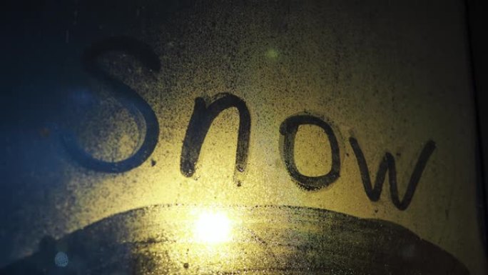 雾蒙蒙的窗户上的铭文雪。玻璃后面正在下雪。照亮路灯。夜间暴风雪