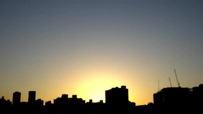 日落风景与城市的建筑轮廓。焦点在正面，背景模糊。镜头轻微晃动。天空的色温接近深蓝色。从右向左倾斜。