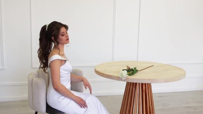 优雅的新娘穿着白色连衣裙，坐着为摄影师摆姿势。